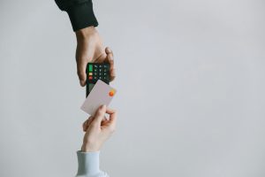 A person handing over a credit card to another person who is holding a payment terminal, demonstrating a traditional card payment transaction.