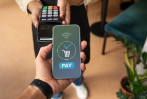 A person holds a smartphone displaying a confirmation screen while making a purchase using contactless digital payments at a point-of-sale terminal.