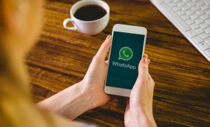 Person holding a smartphone with the WhatsApp logo on screen, illustrating the growing trend of making payments via messaging apps.