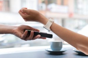 Close-up of a person making payments with wearables by using a smartwatch against a contactless card reader outdoors.