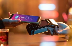 A customer uses a smartphone to complete an instant payment via contactless technology on a card reader at a retail location.