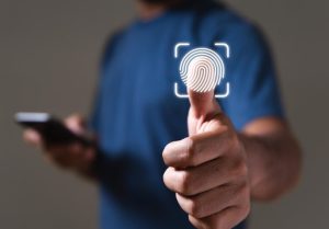A person holds a smartphone while presenting their thumb for fingerprint scanning, illustrating the use of biometric payments for secure authentication.