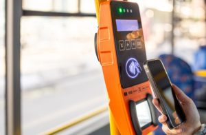 A person using a smartphone to pay at a bus ticket machine, demonstrating the convenience and speed of contactless payments in public transport.