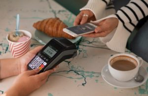 A customer making a contactless payment with a smartphone in a café, illustrating the convenience and security offered by virtual credit cards in everyday transactions.